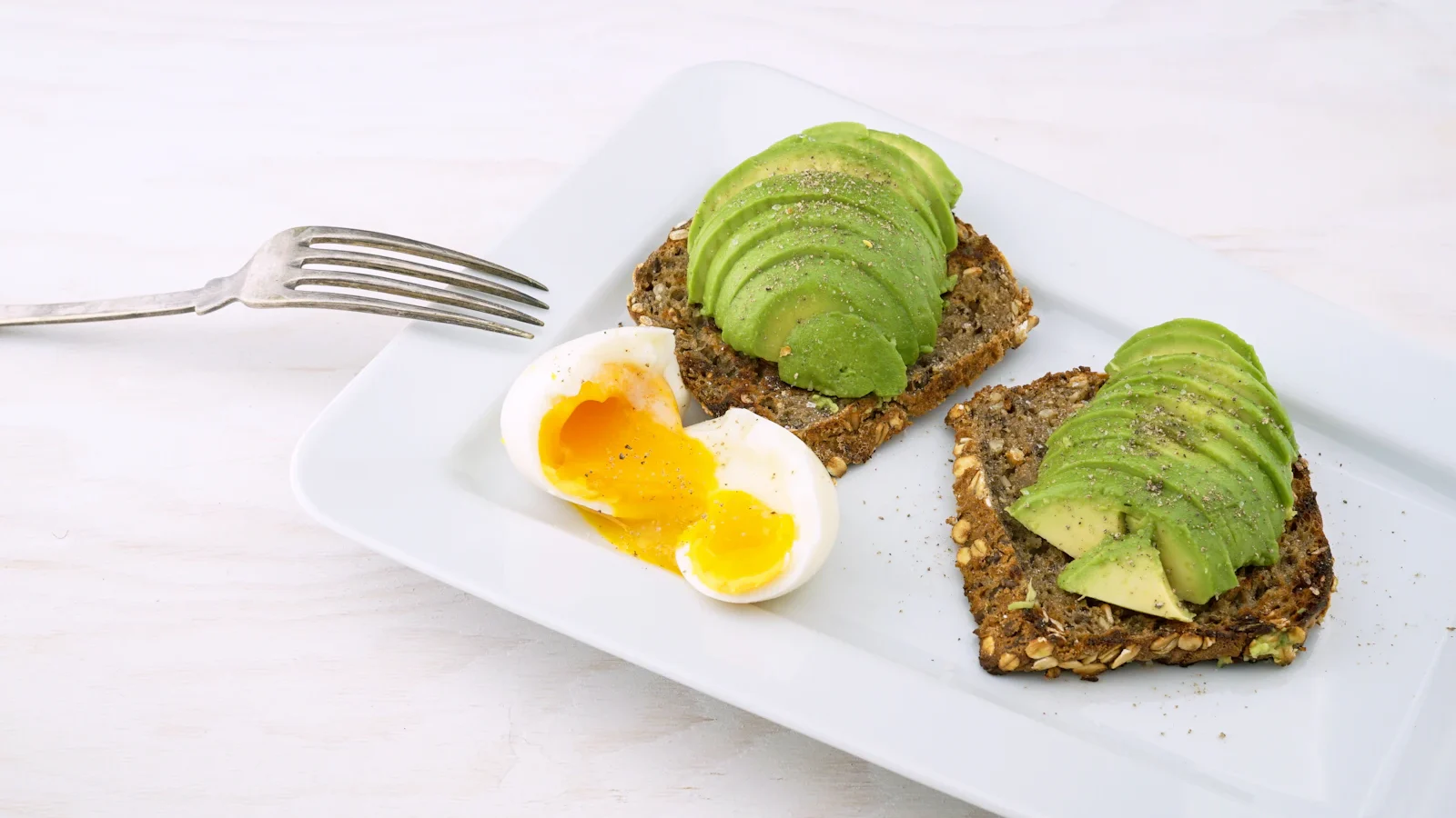 White platter with halved boiled eggs and avocado toast