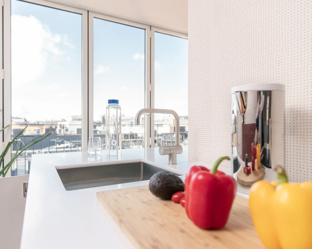 Bright kitchen counter with a cutting board, red and yellow peppers and an avocado beside a sunny window