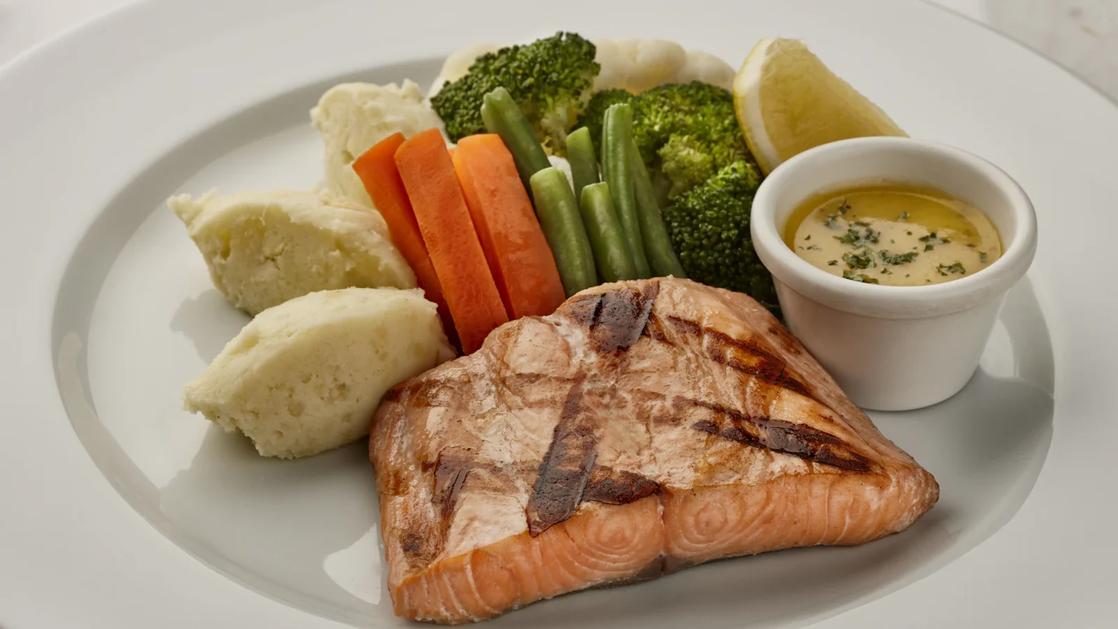 Grilled salmon with carrots, broccoli and potatoes on a white plate