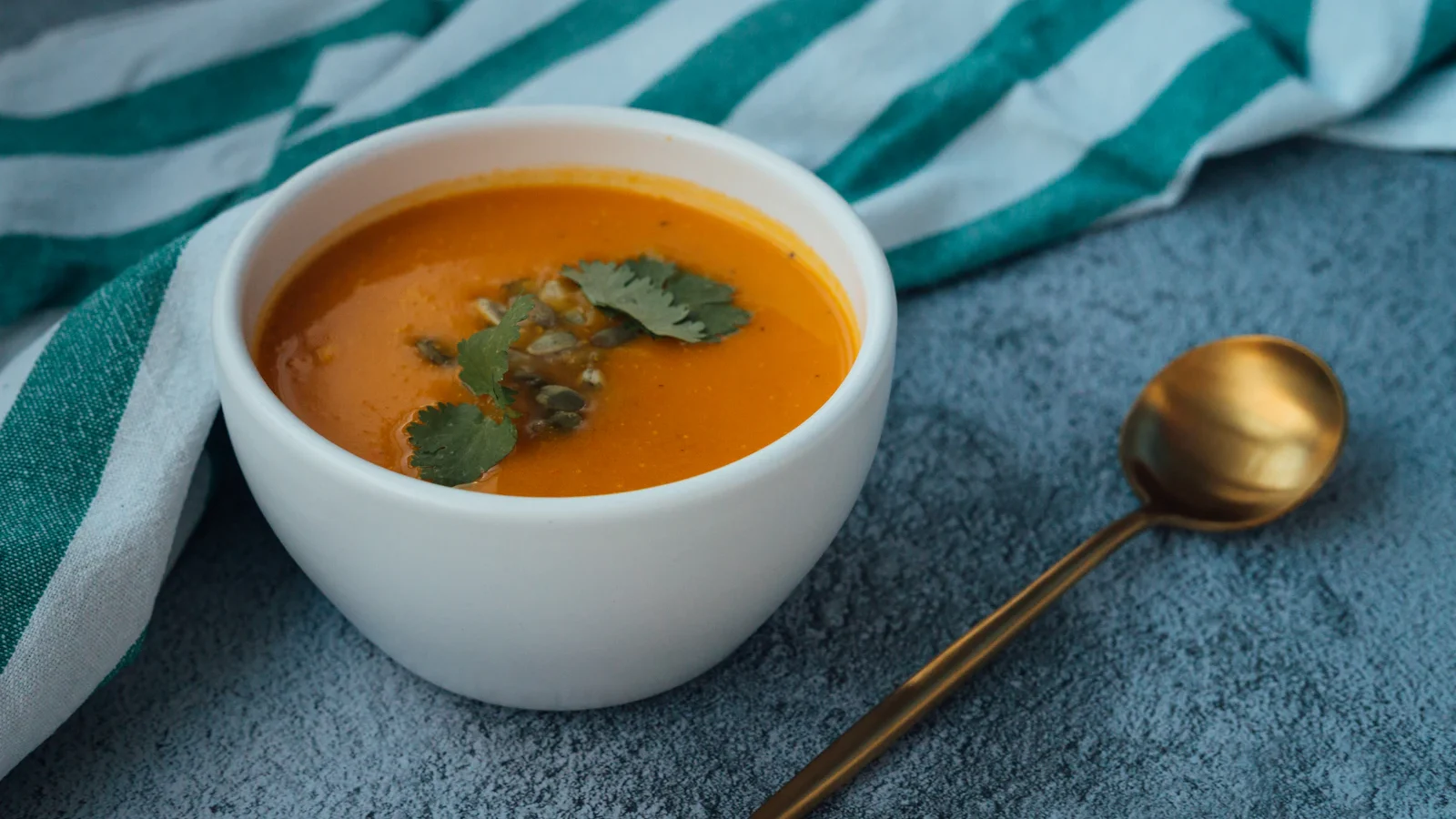 Orange soup in a white bowl with a golden spoon