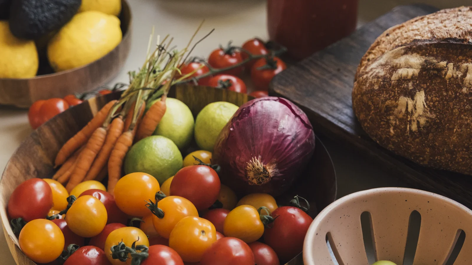 Fresh tomatoes, carrots, avocados and bread on a kitchen counter