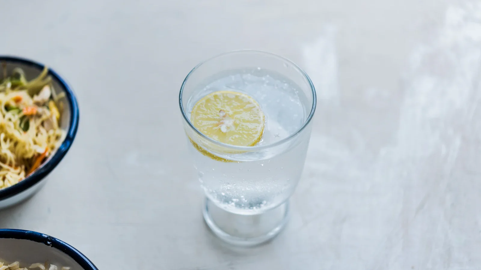 Glass of water with a slice of lemon on a white table