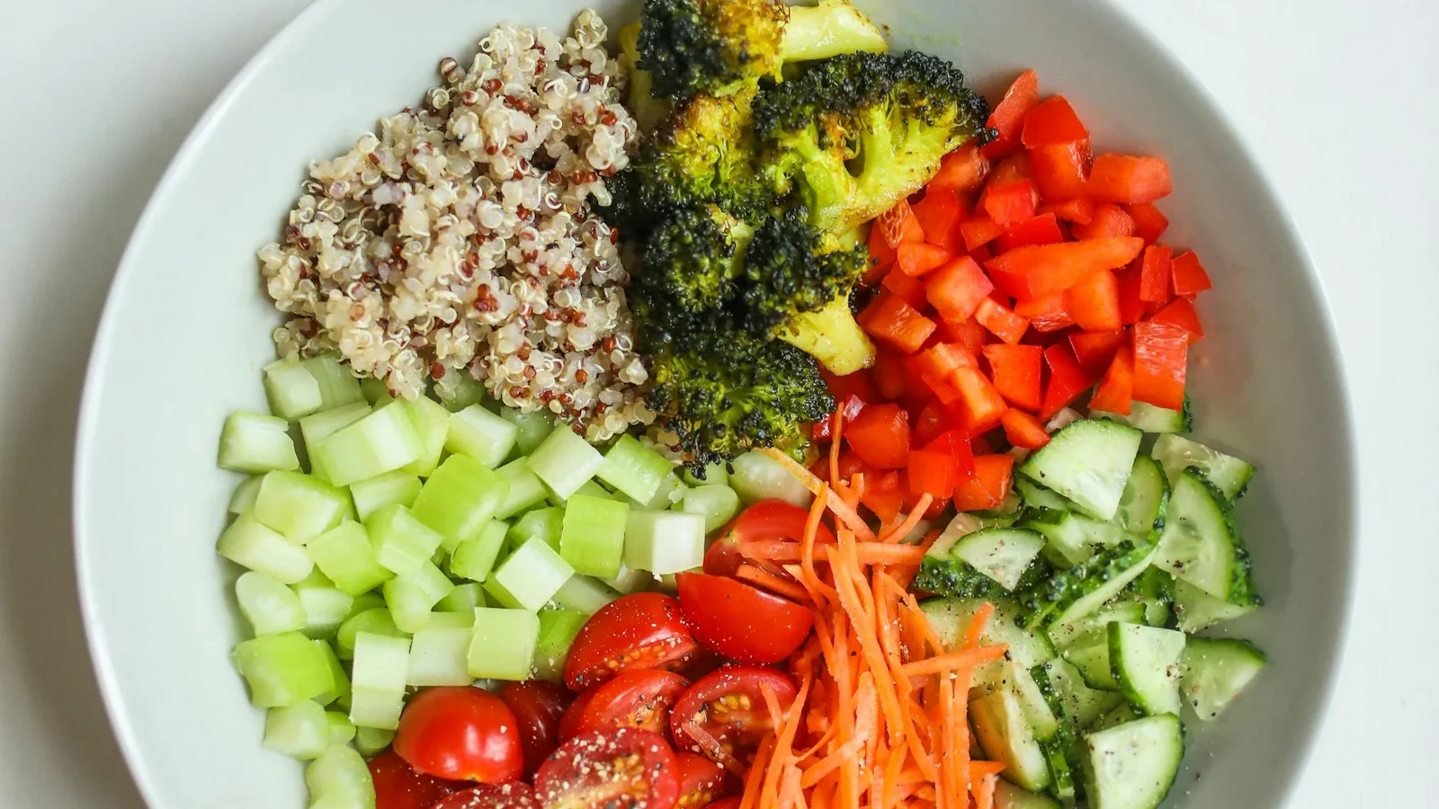 White bowl of quinoa with broccoli, tomatoes, celery and carrot