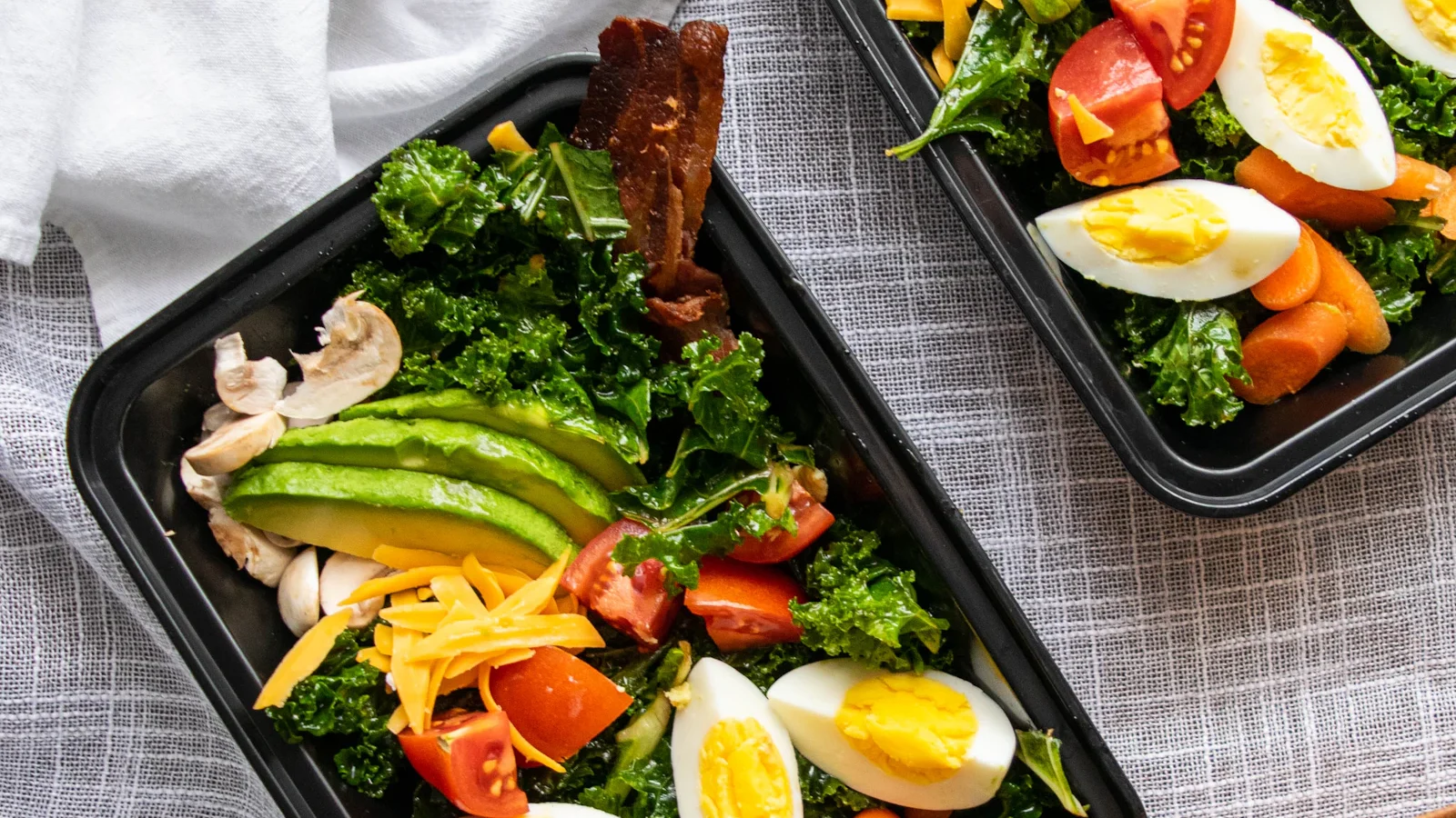 Meal prep trays with chicken, eggs, avocado and salad