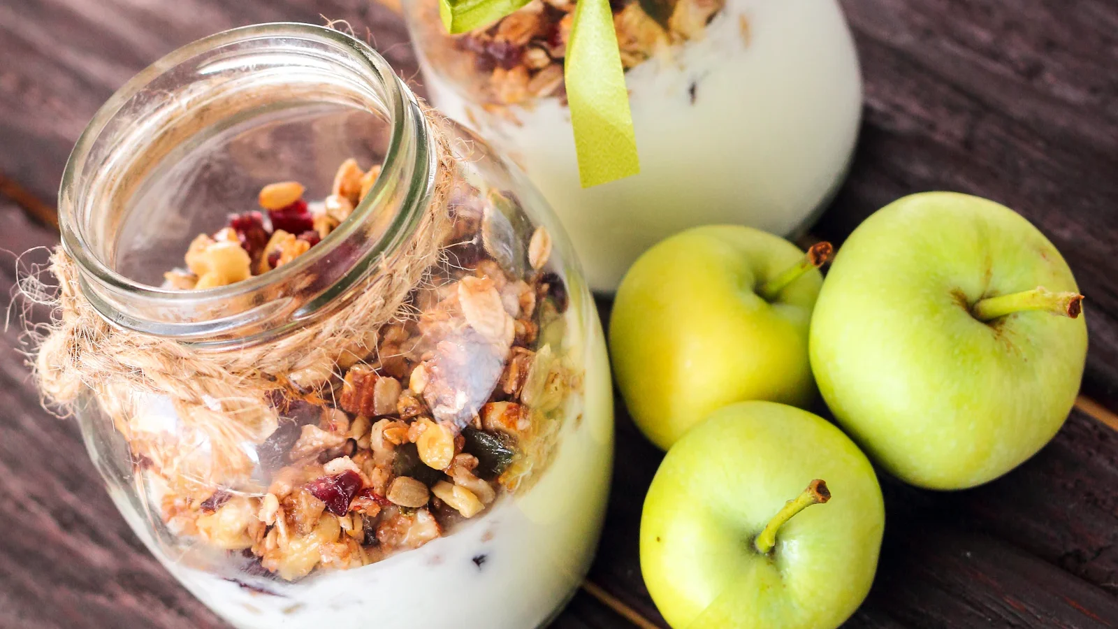 Jar of yogurt and granola next to green apples
